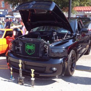 A black truck with the hood open and trophies on top.